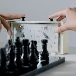Hands Pressing the Button of a Clock Near Chessboard